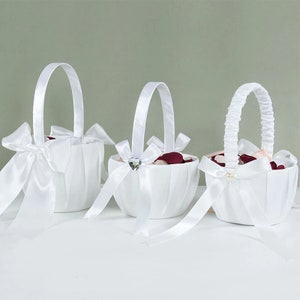 Set of three white satin flower girl baskets with bows and curved handles