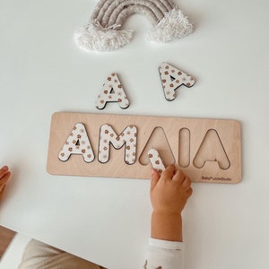 Wooden baby name puzzle board with pastel flower letters and hand holding piece
