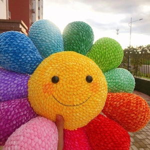 Crochet smiling flower pillow with yellow face, green petals, red and purple accents