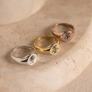 Birth flower signet rings in silver and gold, each with small black flower detail
