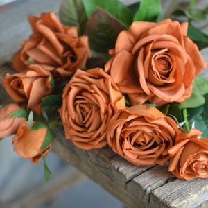 Orange faux rose bouquet with dark green leaves on a rustic wooden base