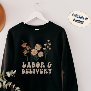 Black sweatshirt with floral daisies and “LABOR & DELIVERY” text on front