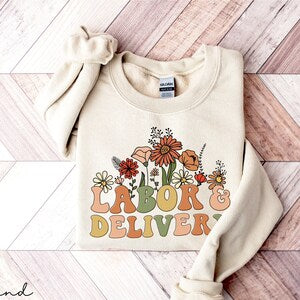 Cream crewneck sweatshirt with colorful floral “Labor & Deliver” front graphic