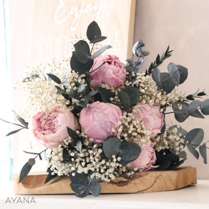 Dried pink peony and baby's breath bouquet with dark eucalyptus leaves on wood base