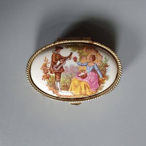 Vintage oval pill box with gold-tone rim and painted courting lovers scene