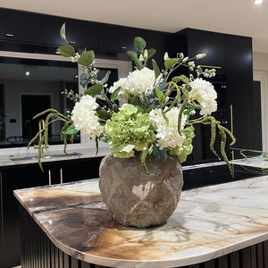 Green and white faux flower arrangement in a textured stone-look vase centerpiece