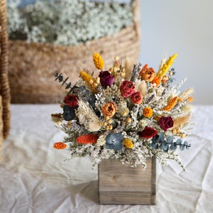 Boho dried flower centerpiece in a wooden box with orange, burgundy, and blue blooms