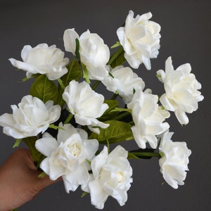 White artificial gardenia flower cluster with green leaves, realistic textured petals