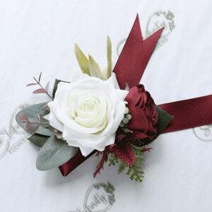 Artificial wrist corsage with ivory rose, burgundy ribbon, and green foliage