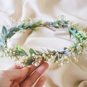 Green floral wreath crown with small white baby’s breath-style blooms and greenery