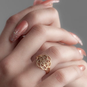 Silver openwork flower-of-life ring with gold-toned center on finger