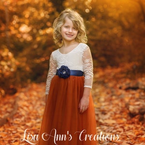 Rust orange flower girl dress with lace bodice, navy sash, and large fabric flower