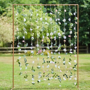 Hanging flower curtain backdrop with white blossoms and green foliage on a gold frame