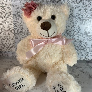 Cream plush teddy bear with pink satin bow; “Flower Girl” and “Kitty” embroidered on paws