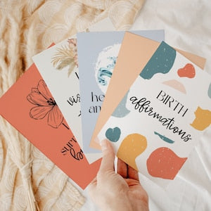 Set of birth affirmation cards, colorful illustrated designs with text, held in hand