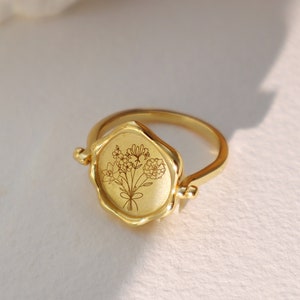 Gold-tone birth flower ring with oval floral engraving and small side accents