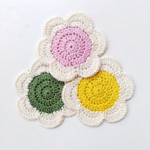 Crochet flower coaster with pink and yellow centers and green leaf petals