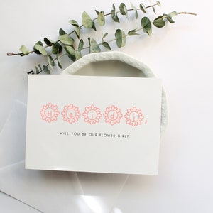 White flower girl proposal card with pink border and 'Will you be our flower girl?' text