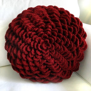 Round crocheted pillow cover in dark red, textured flower-like spiral knit.