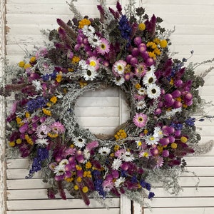 Round dried flower wreath with purple blooms, white daisies, and yellow accents