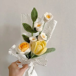 Crochet flower bouquet with white and yellow blooms and green leaves, wrapped in ribbon