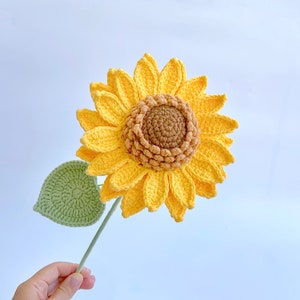 Sunflower crochet flower with textured yellow petals and green leaf on a stem