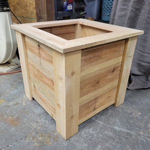 Natural wood planter box with slatted sides and wide top rim, corner joints visible