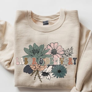 Off-white crewneck sweatshirt with colorful floral 'Labor & Delivery' graphic on front