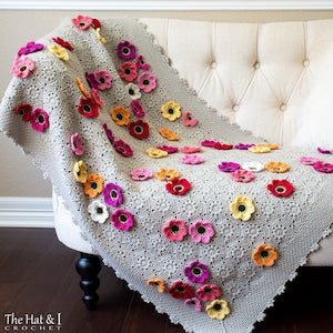Gray crochet blanket with colorful crocheted flower motifs and scalloped edging