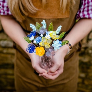Colorful glass flower bouquet with blue, yellow, and green blooms and leaves.