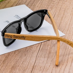 Kids sunglasses with black frames, dark lenses, and wooden arms with ring security strap