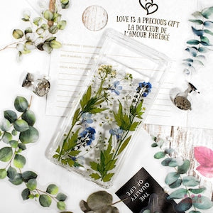Pressed flower phone case cover with blue and green dried botanicals on clear background