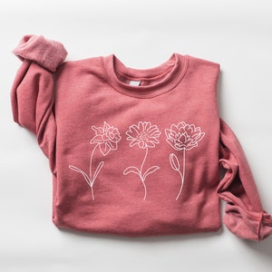 Pink crewneck sweatshirt with white line flower graphic across the chest
