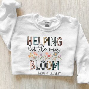 White labor and delivery sweatshirt with "HELPING little ones" and "BLOOM" graphic