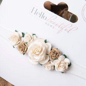 Baby flower headband with cream rosette flowers and green leaf accents on a white band