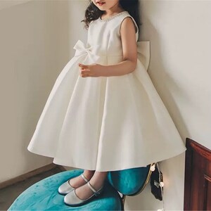 Ivory satin tea-length baby girls dress, sleeveless bodice with bow detail, full skirt