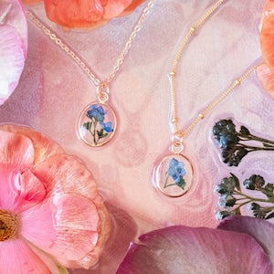Pressed flower necklace with round blue floral pendant on a gold chain