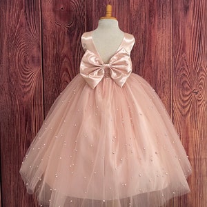 Blush tulle flower girl dress with satin bow, V-back bodice, ankle-length skirt.