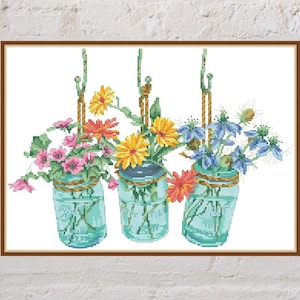 Cross-stitch pattern of three floral jars with multicolor flowers on teal jar drawings