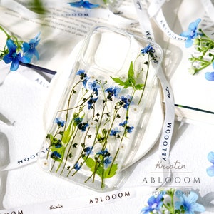 Handmade pressed flower phone case with clear back, blue and white blooms, green stems
