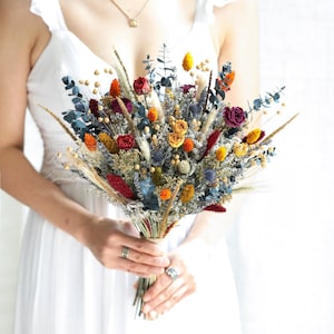 Boho dried flower bouquet with orange, yellow, blue blooms and greenery, held by hands