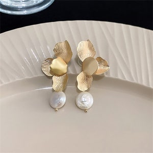Gold flower drop earrings with white pearls and layered petal design.