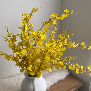 Yellow artificial flower branch with small blossoms in a white vase