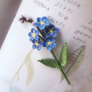 Crocheted mini flower bouquet with blue and yellow blossoms, purple accents, and green leaves