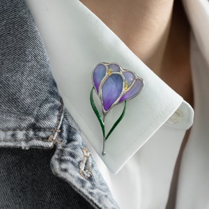Stained glass flower brooch pin with purple bloom and green stem on a white shirt