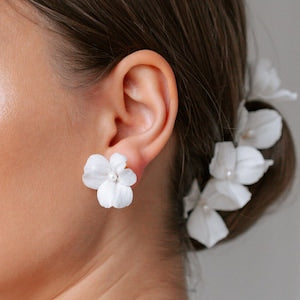 White floral stud earrings with layered petals, worn on ear