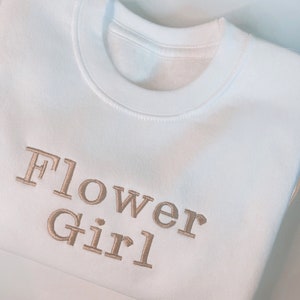 Light cream crewneck embroidered sweater with Flower Girl text in gold brown
