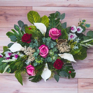 Artificial cemetery flower arrangement with red/pink roses, white calla lilies, and green leaves