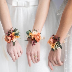 Orange and peach floral wrist corsage with ribbon, worn on a bridesmaid's wrist