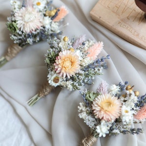 Peach and cream dried flower boutonniere with small white blooms and greenery